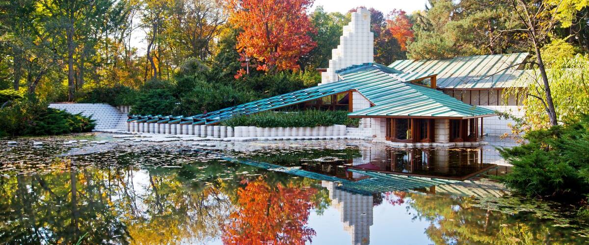 A traditional Japanese garden with a stone bridge, a pond with lotus flowers, and autumn-colored trees.