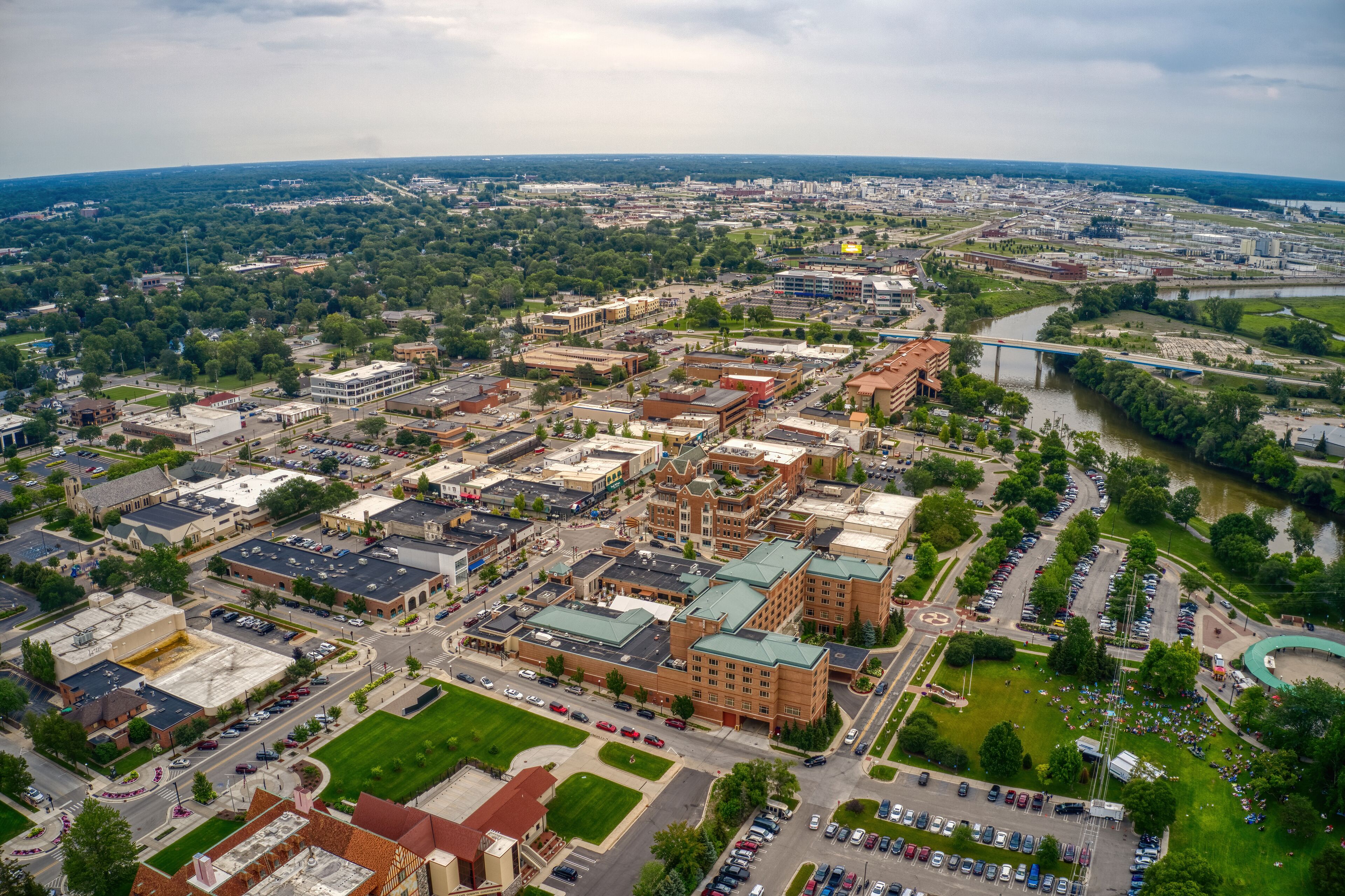 An aerial view of a city with a river, green spaces, and various buildings.