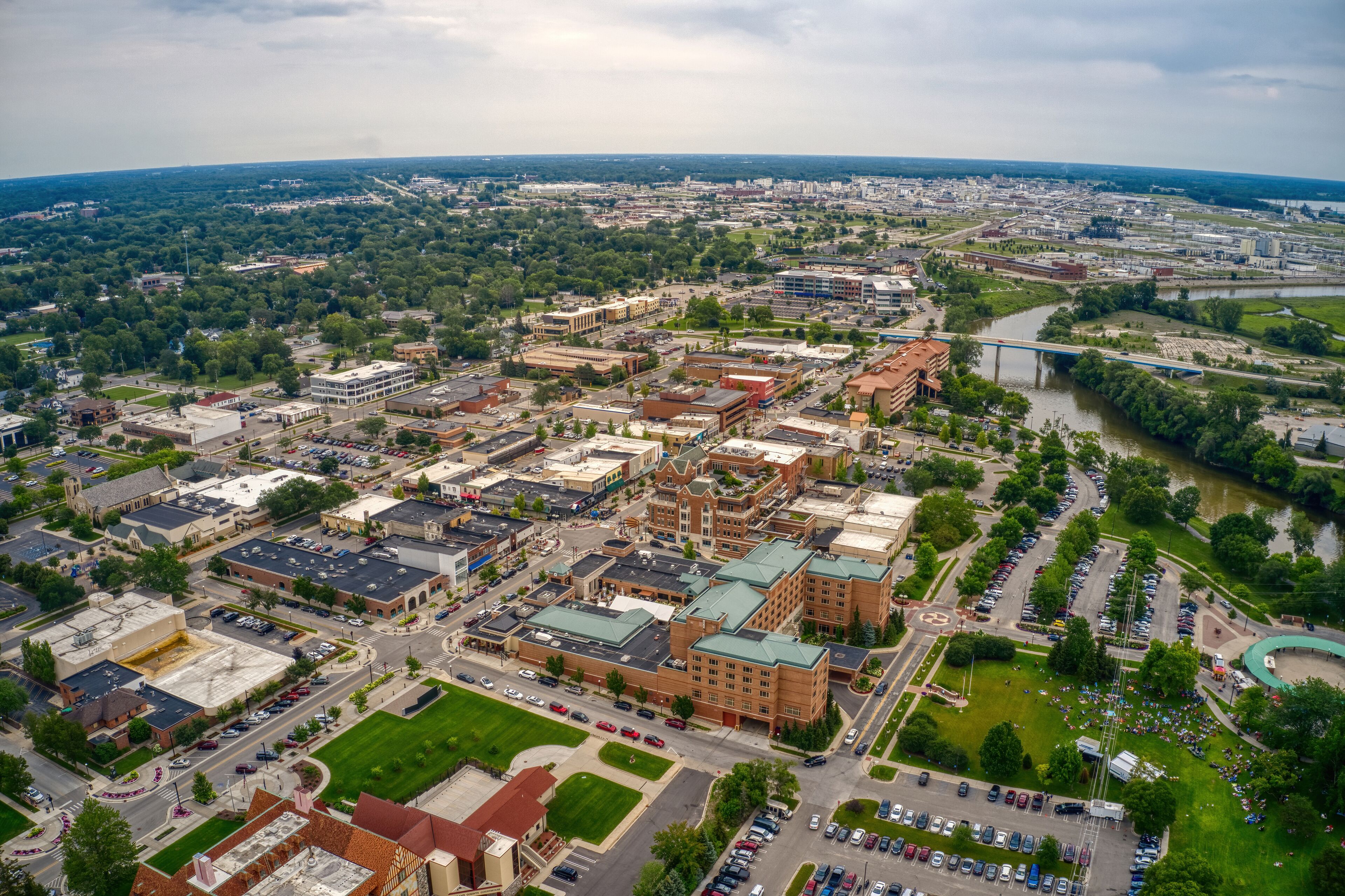 An aerial view of a city with a river, green spaces, and various buildings.