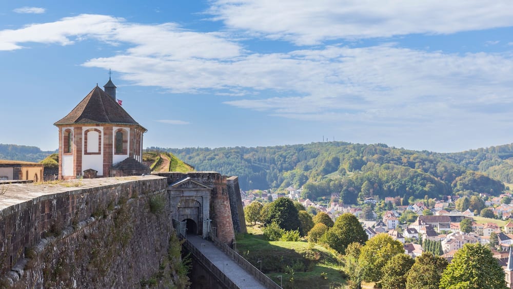 Un mur de pierre d’époque, une église dotée d’un clocher et une ville située dans la vallée en contrebas.