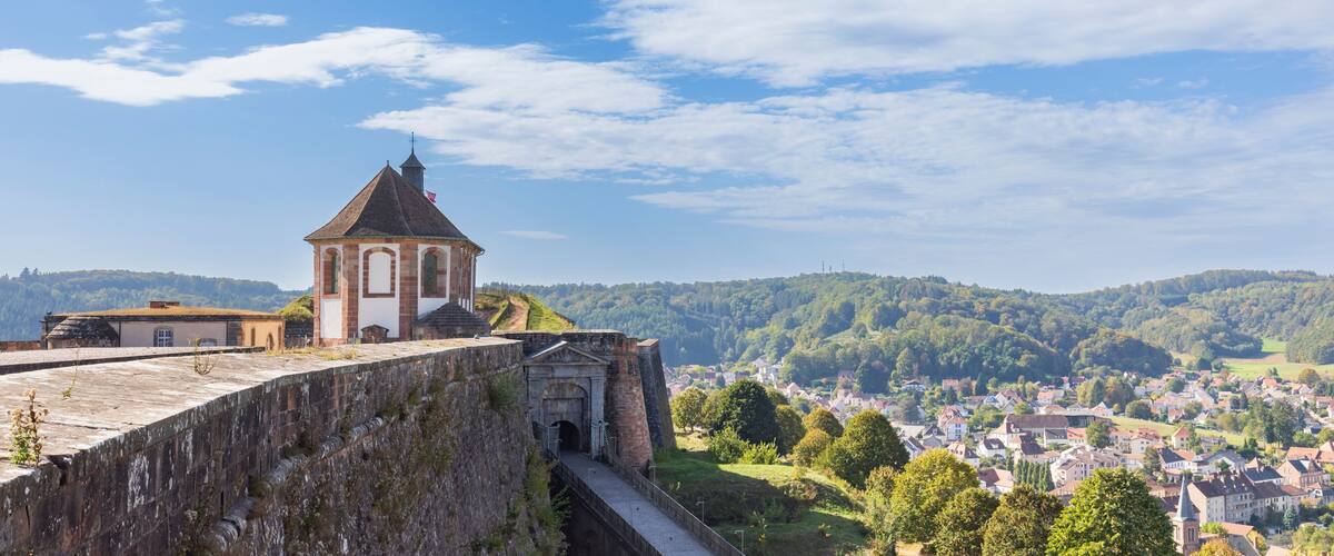 A historic stone wall, a church with a bell tower, and a town in the valley below.
