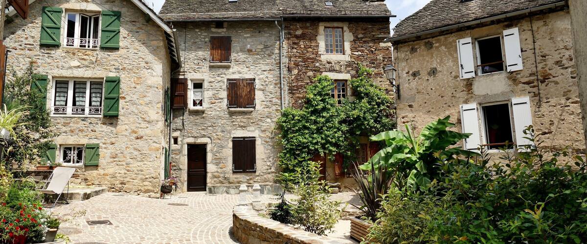 A cobblestone courtyard surrounded by stone buildings with green shutters.