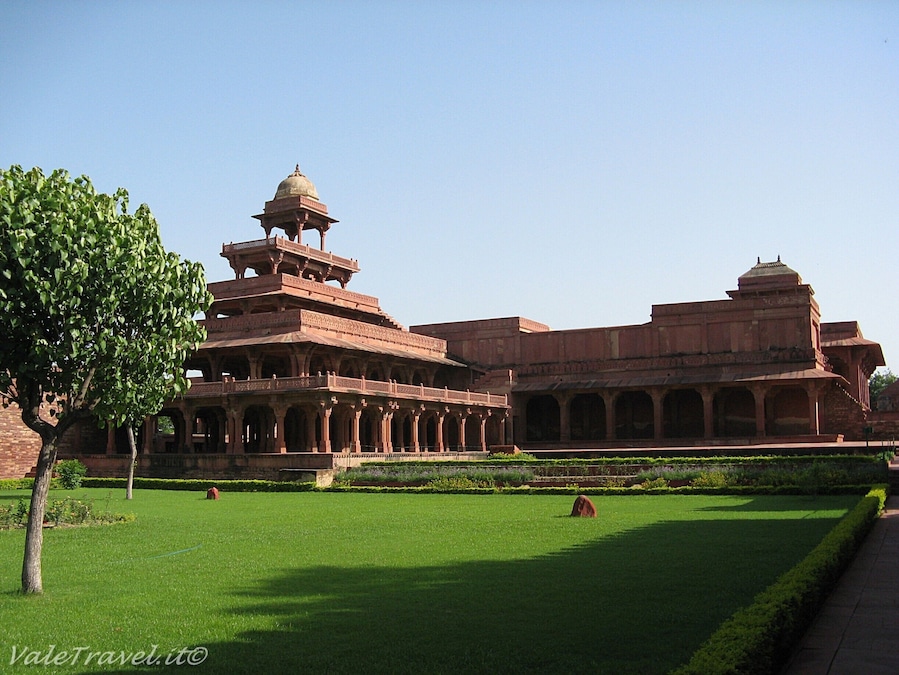 A large, historic building with a central dome and multiple smaller domes, surrounded by well-maintained green lawns and a few trees.