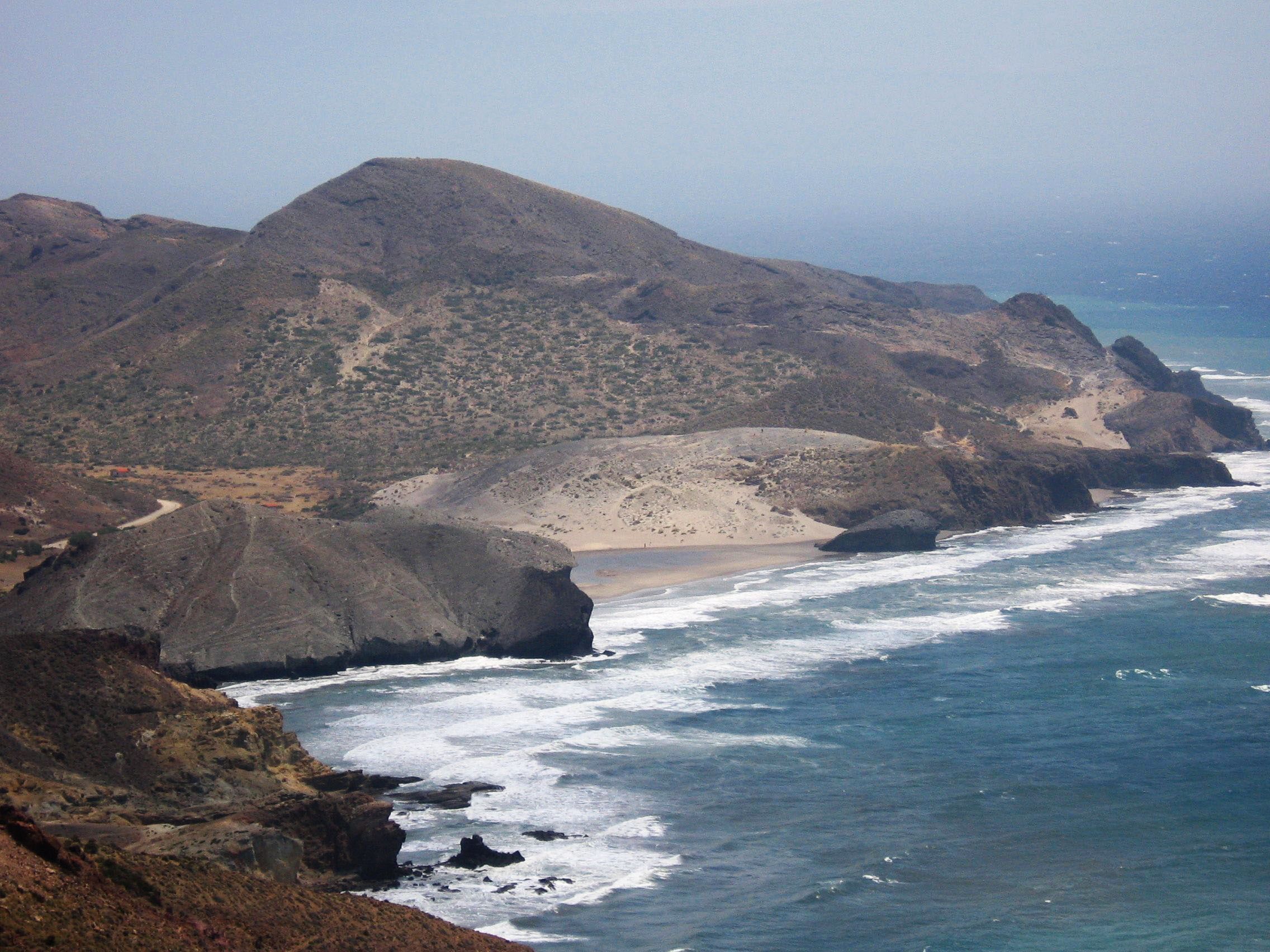 A coastal landscape with rocky cliffs, a sandy beach, and waves crashing against the shore.