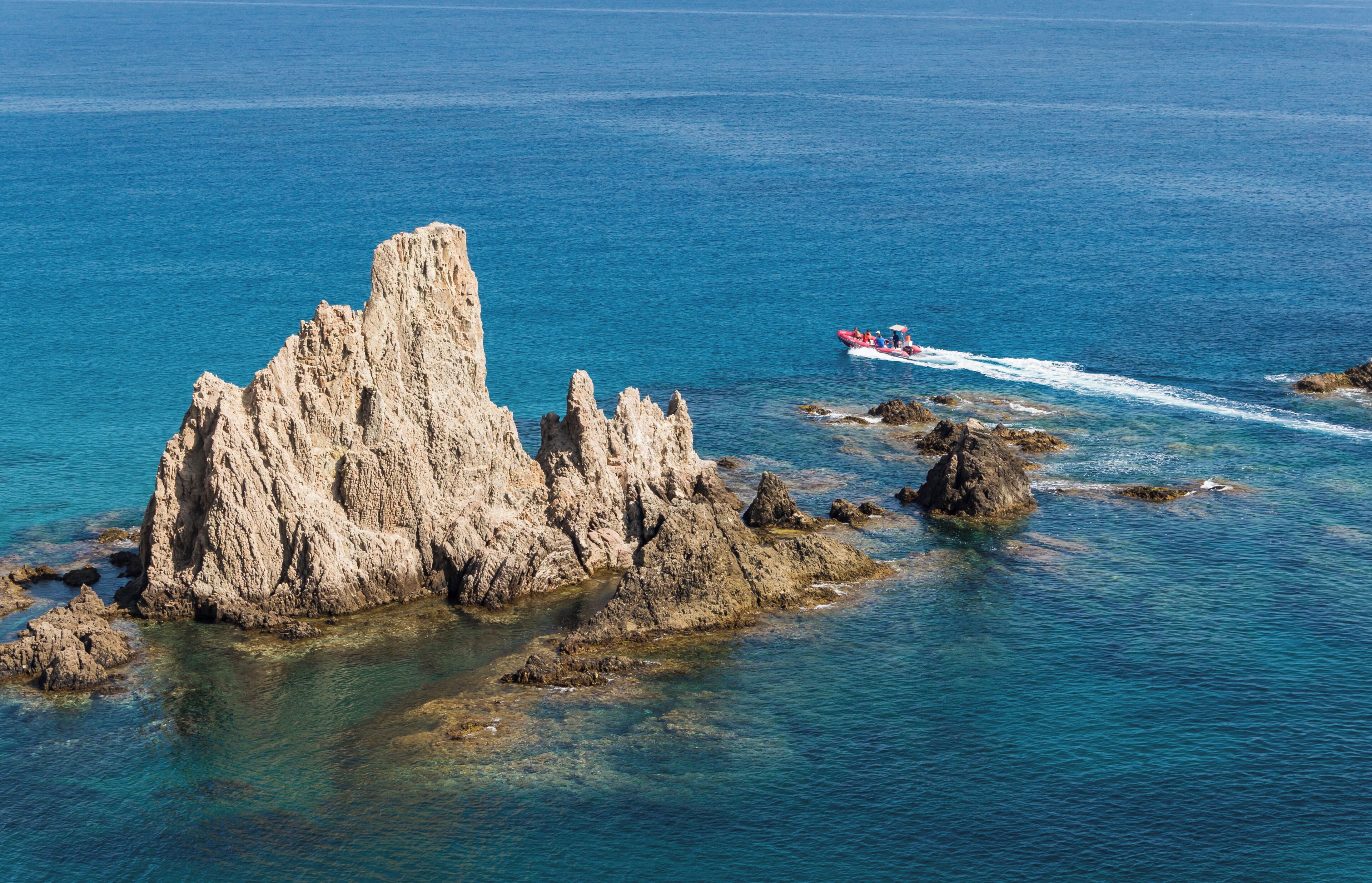A rocky coastline with clear blue waters and a small boat with people on it.