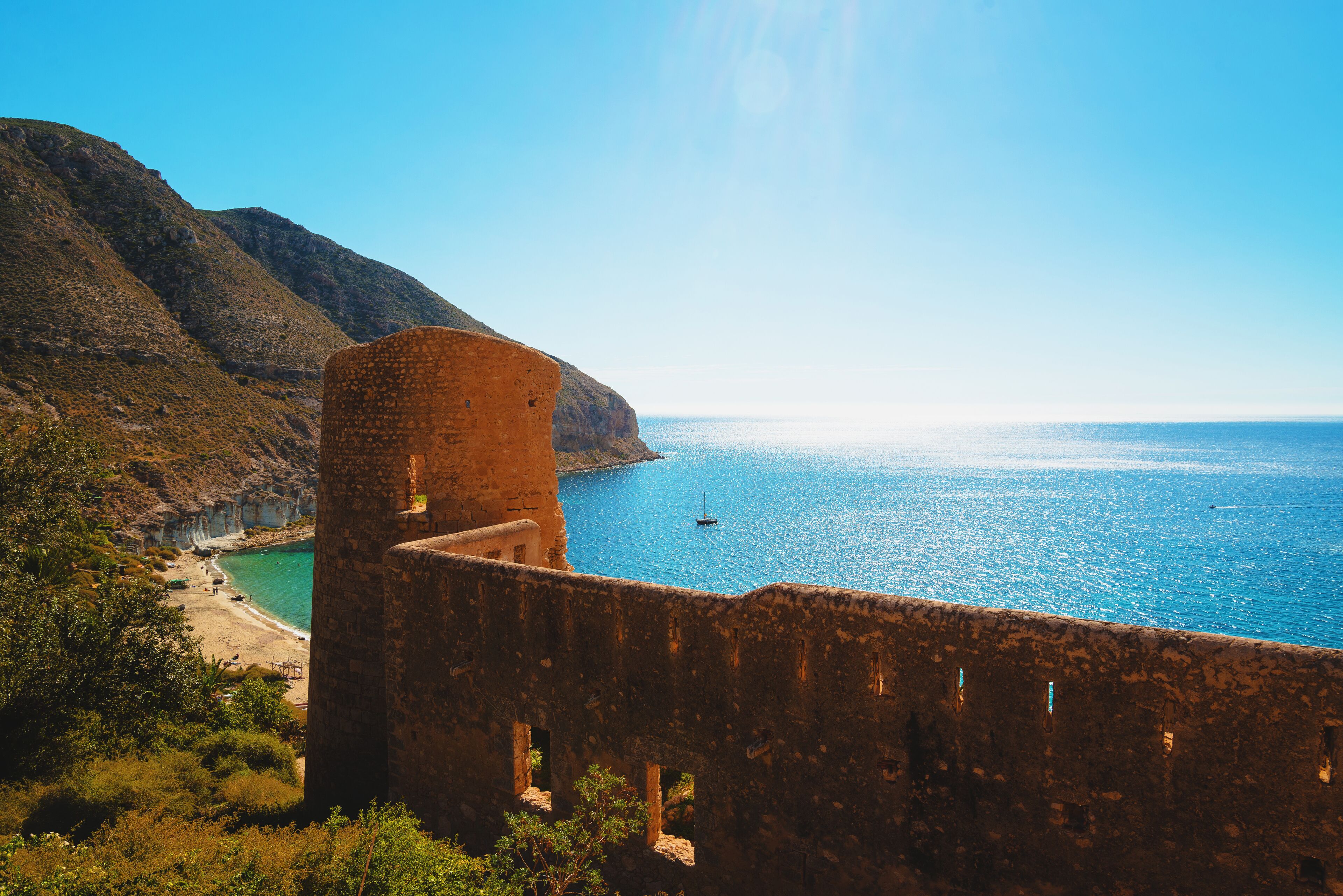 A coastal landscape with a historic stone tower overlooking a beach and the sea.