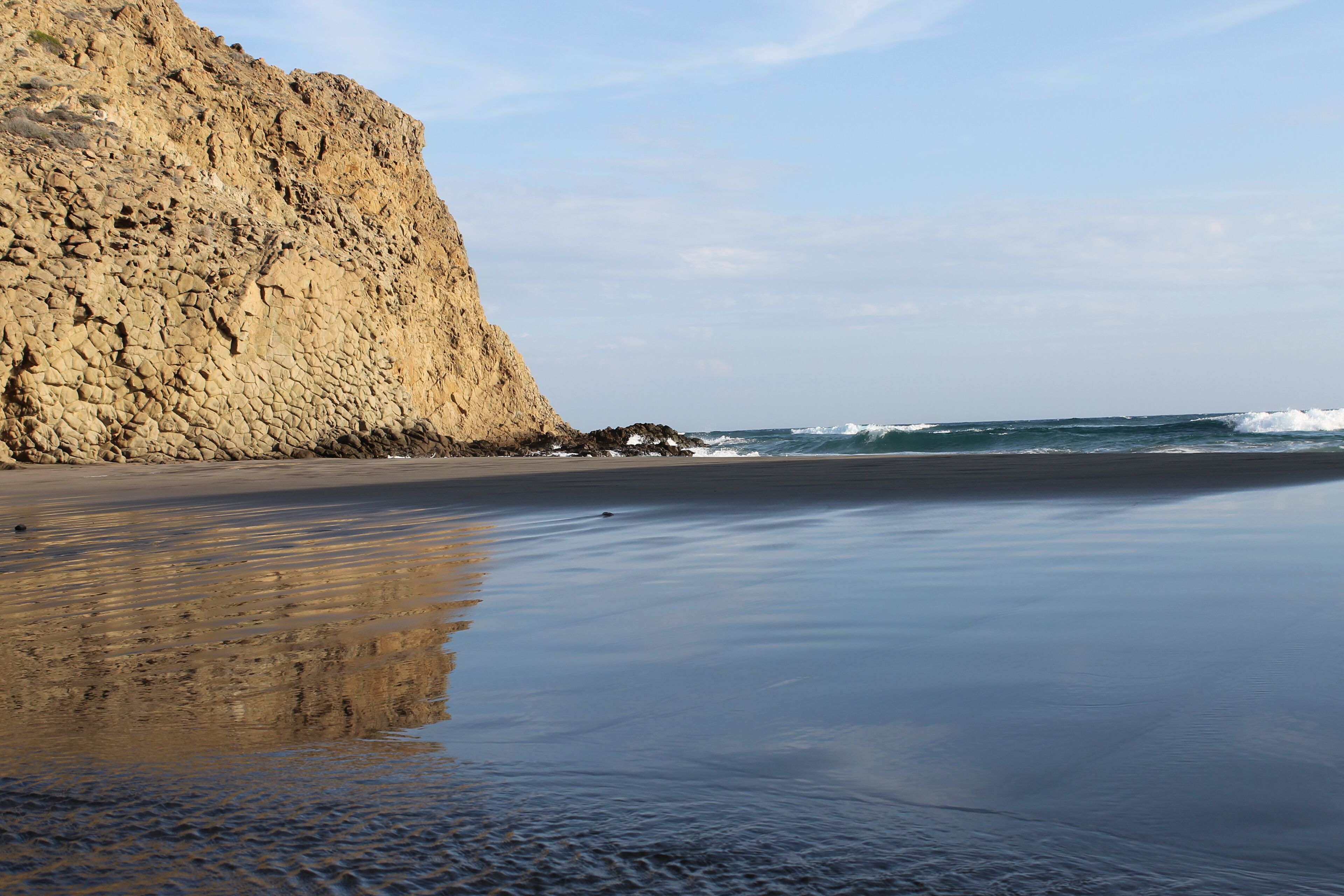 A rocky cliff, a sandy beach, and ocean waves.