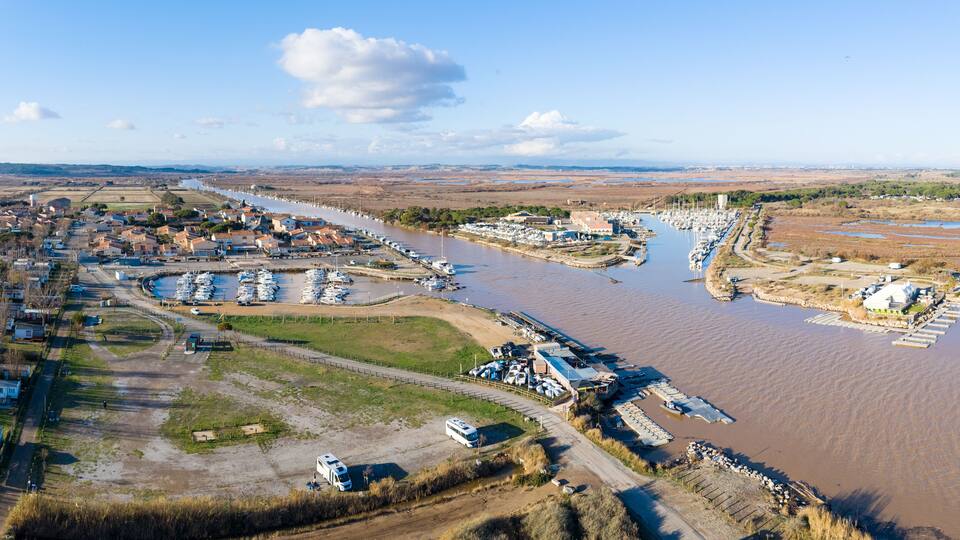 An aerial view of a riverside town with a marina, boats, and industrial buildings.