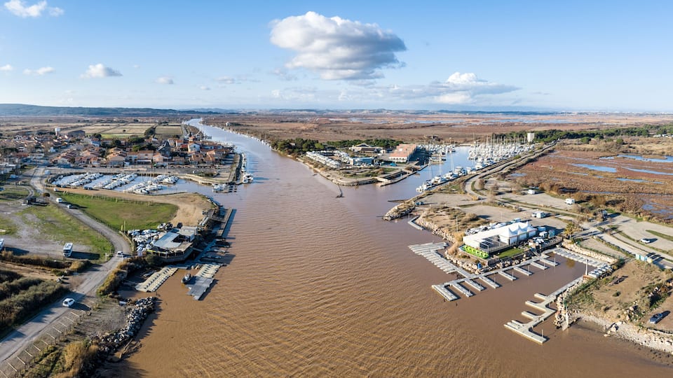 A river with boats, a marina, and a town with buildings and vehicles.