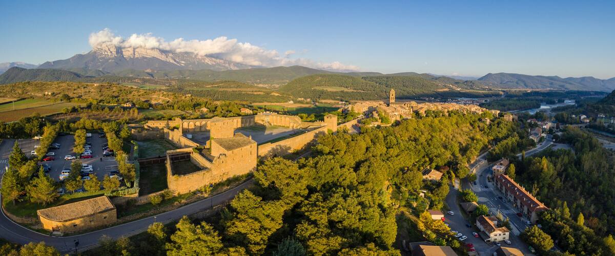 A mountainous landscape with a historic fortress, a river, and a town.