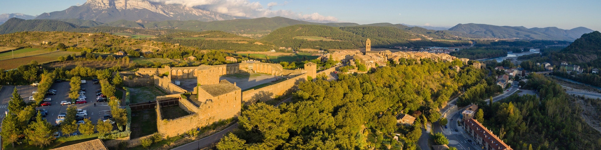 A mountainous landscape with a historic fortress, a river, and a town.