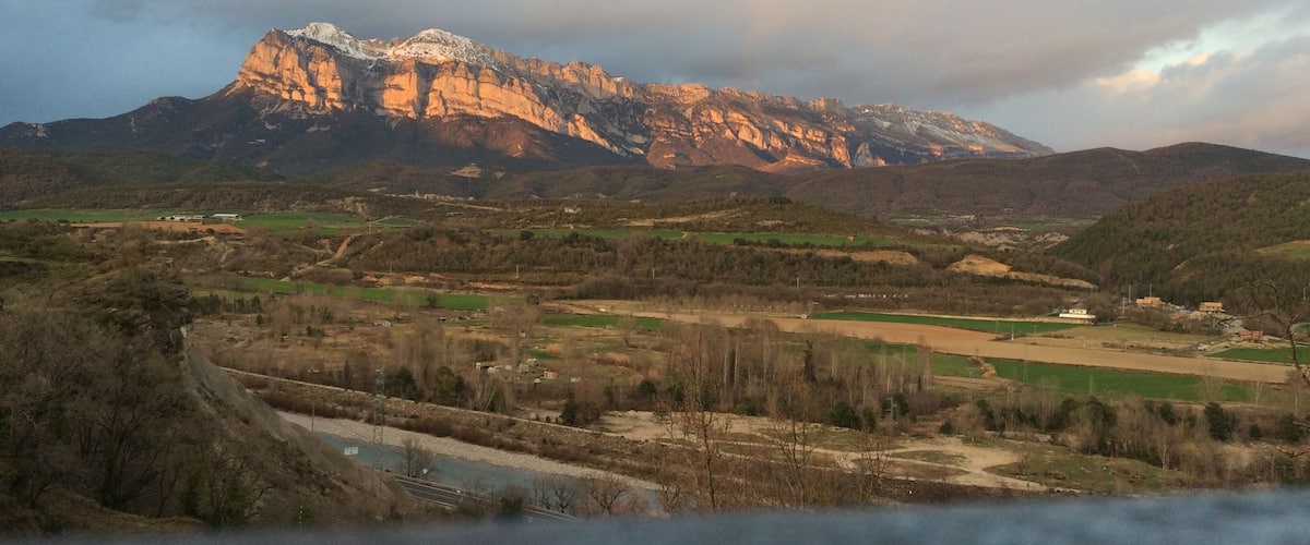 A mountainous landscape with a river, fields, and sparse trees.