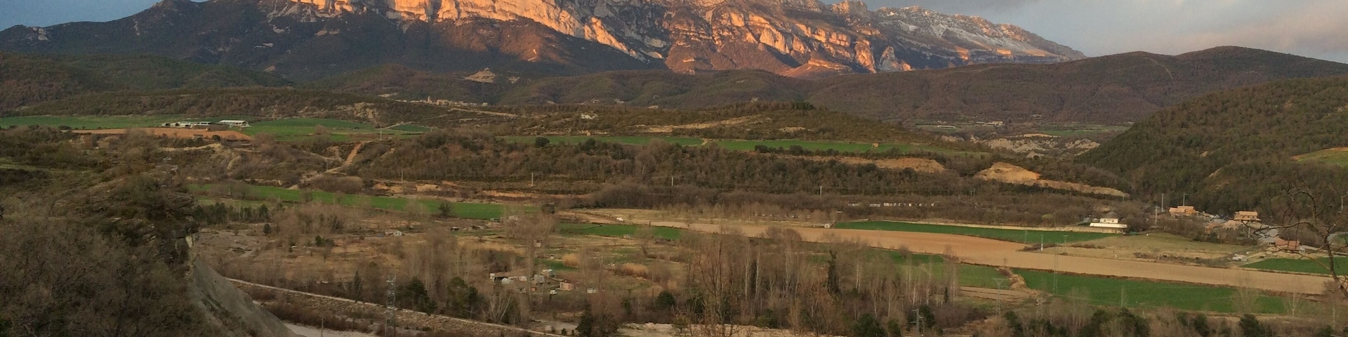A mountainous landscape with a river, fields, and sparse trees.