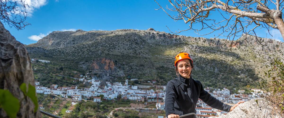 A person rappelling down a rocky cliff with a town in the background.
