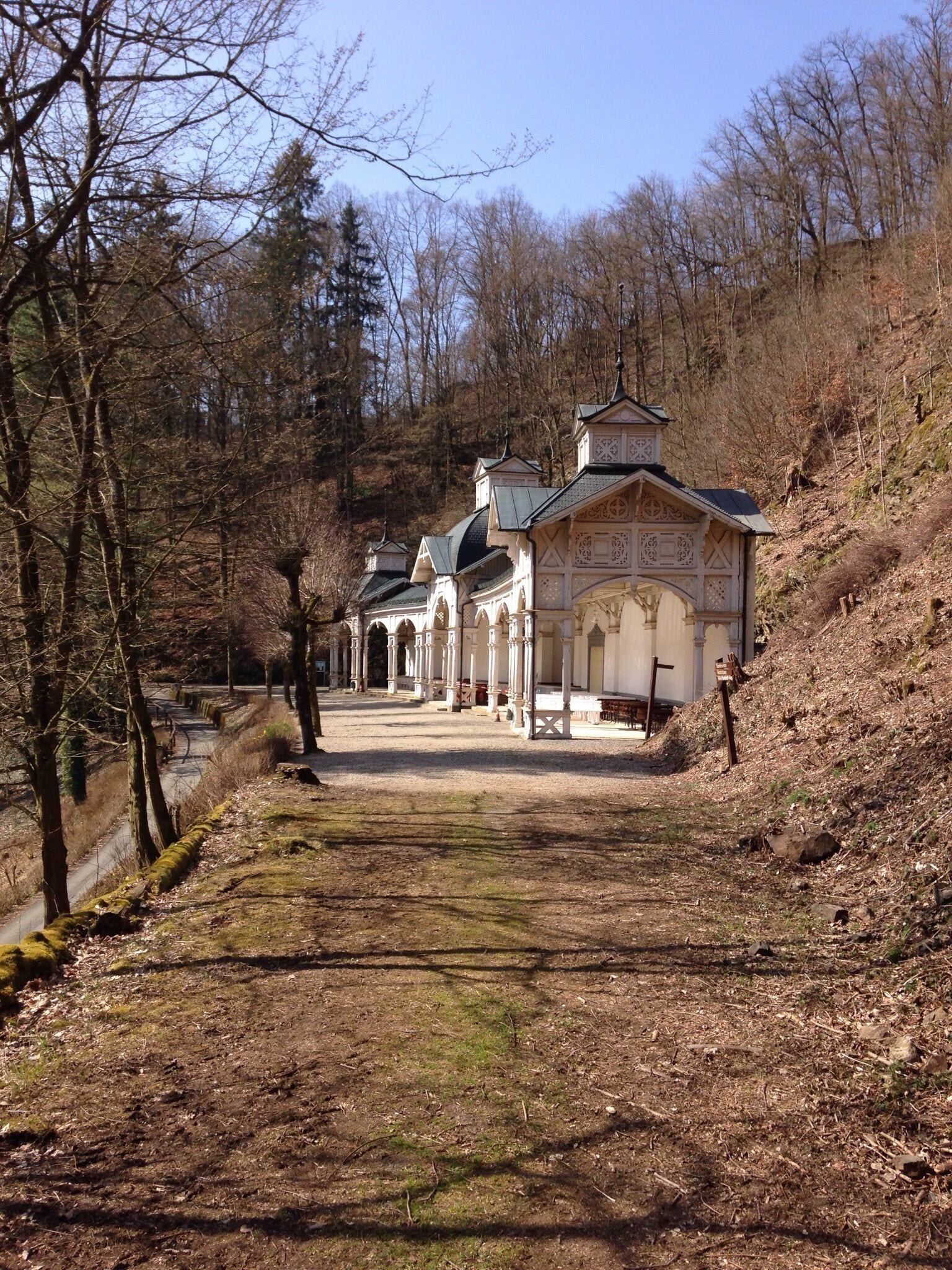 A pathway leading to a series of traditional buildings with ornate architecture, surrounded by a forested landscape.