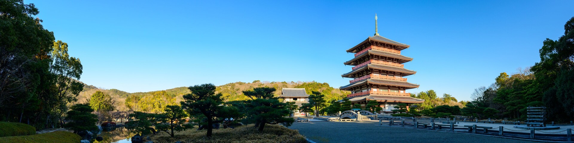 Una pagoda japonesa tradicional con varios niveles, rodeada por un paisaje sereno con un estanque y árboles bien cuidados.