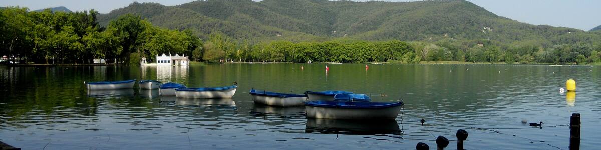 Un lac paisible où sont amarrés plusieurs petits bateaux près du rivage, entouré de collines verdoyantes et sous un ciel dégagé.