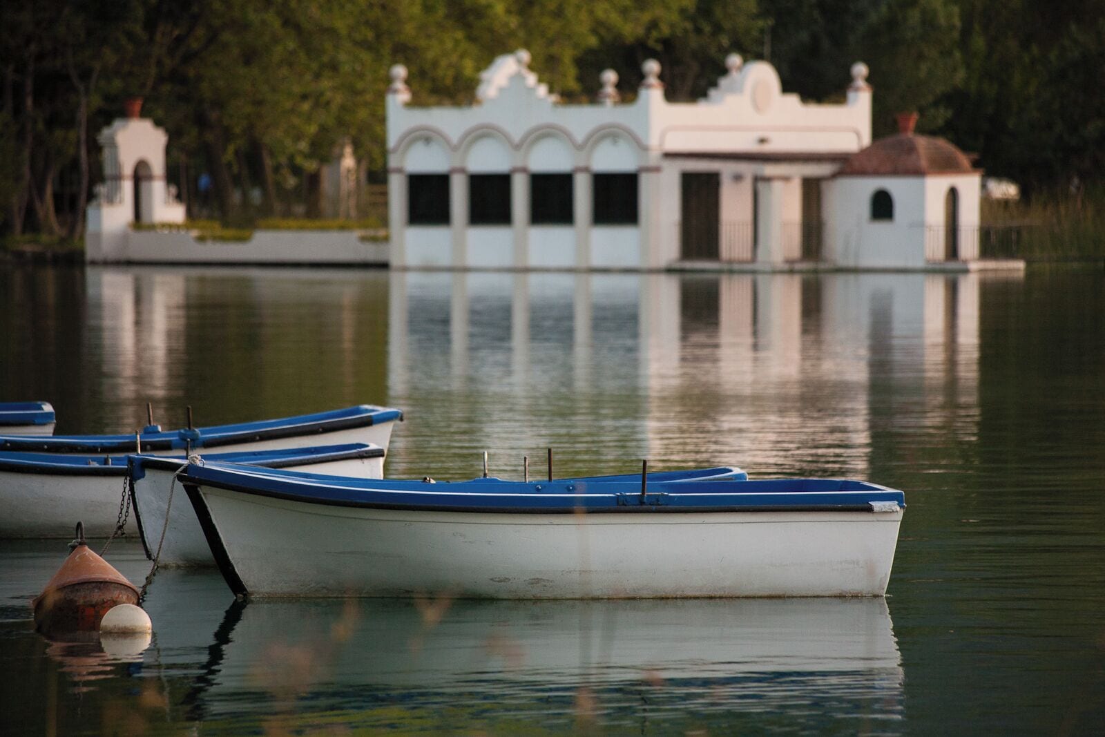 A rowboat tied to a buoy near a white building with a dome roof.