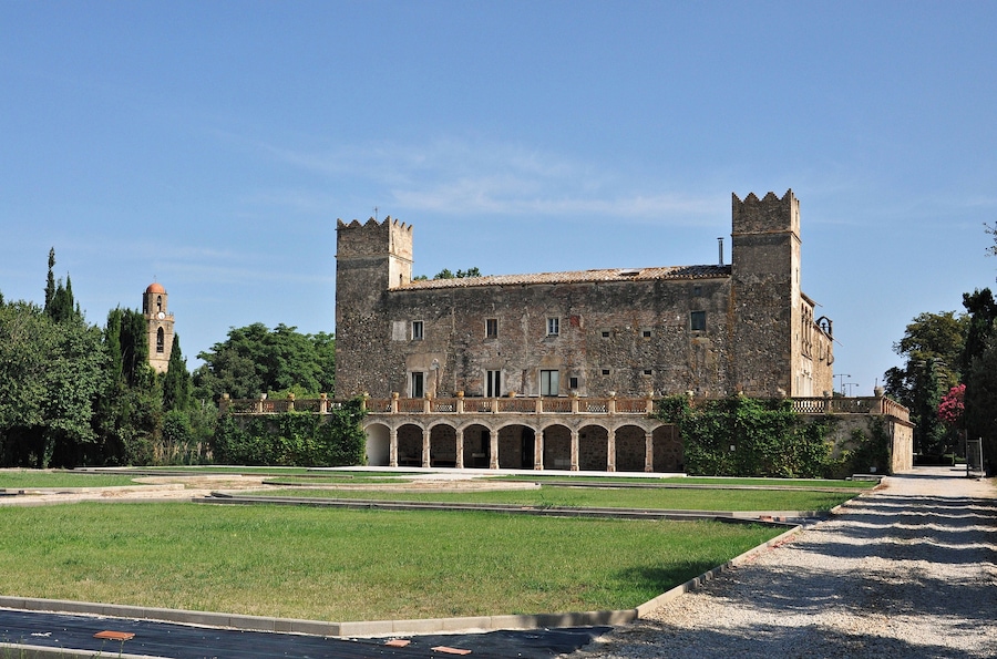 A historic stone building with two towers, a courtyard, and surrounding greenery.