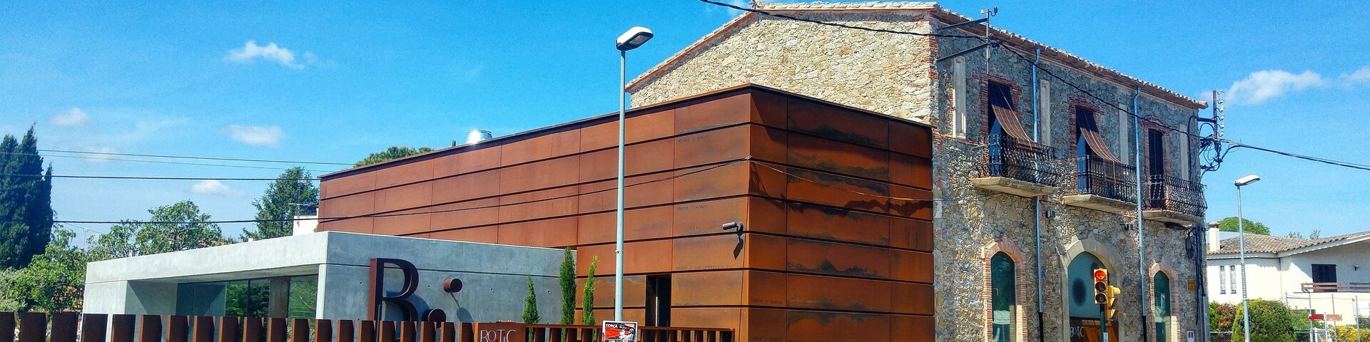 A building with a modern facade and a stone base, a metal fence, and a clear blue sky.