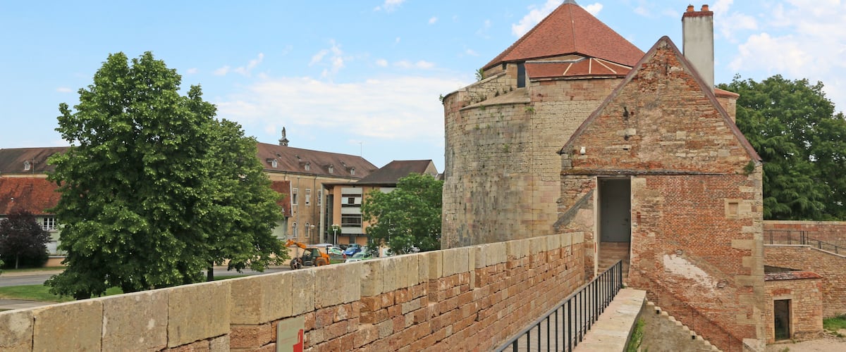 A historic stone tower with a red roof, a brick wall, and a metal railing.