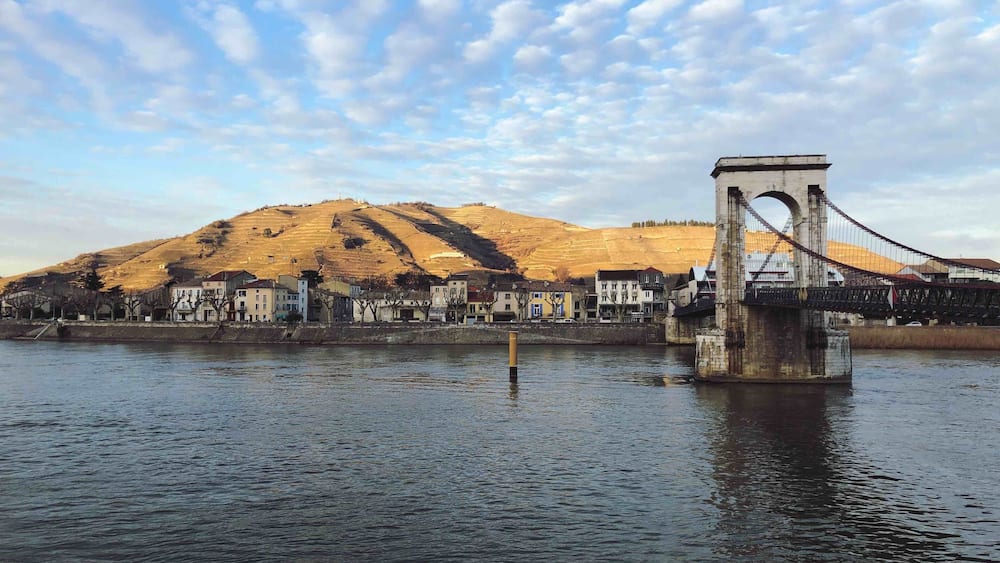 Un pont enjambant une rivière, avec des bâtiments et une colline en arrière-plan.