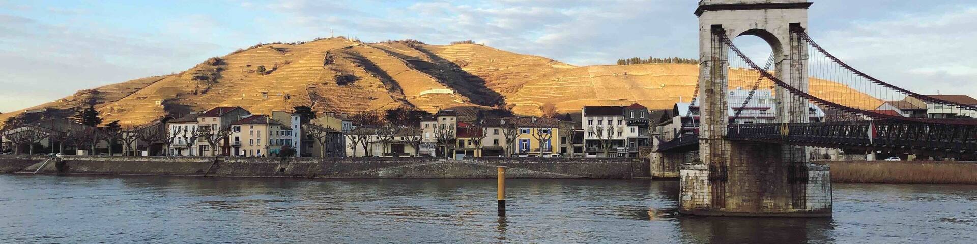 A bridge over a river with buildings and a hill in the background.