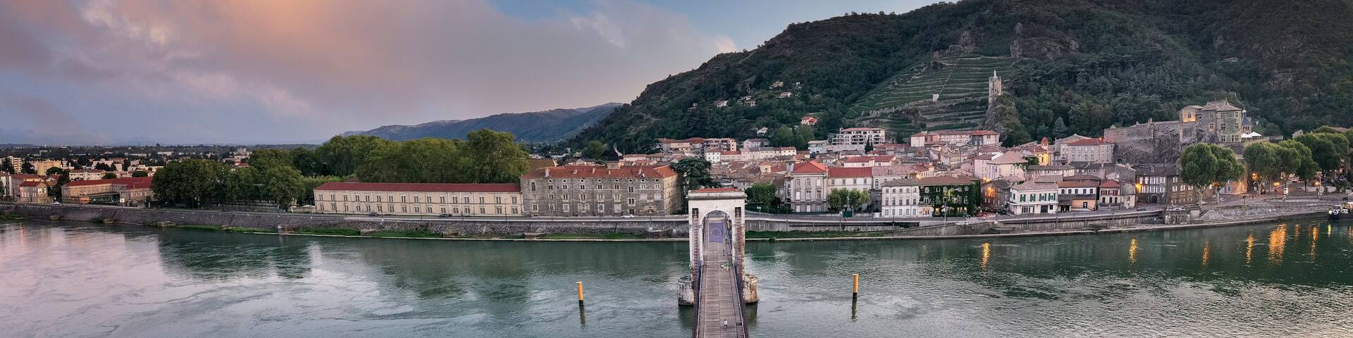 A river with a bridge, a town with historic buildings, and a hill with a church.