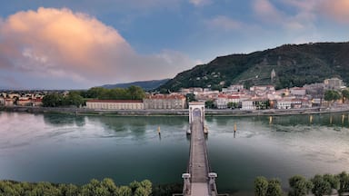 Une rivière traversée par un pont, une ville avec des bâtiments historiques et une colline surmontée d’une église.