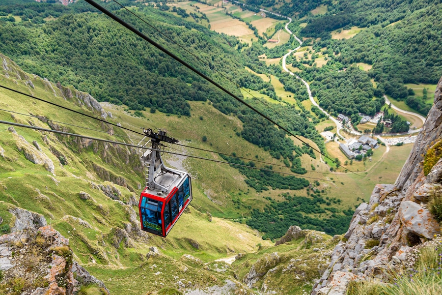 Um teleférico suspenso sobre uma paisagem montanhosa com vegetação exuberante e estradas sinuosas abaixo.