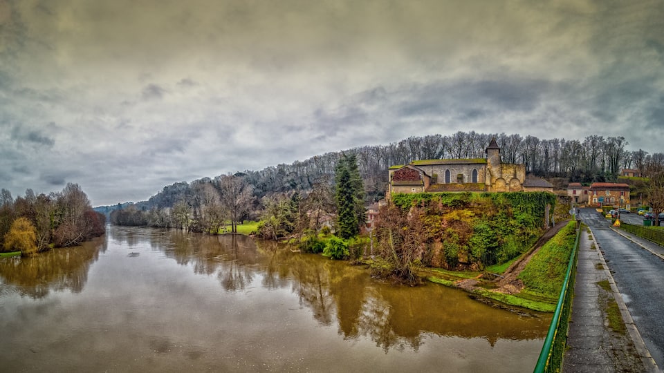 A river with a church on a hill and a road alongside.