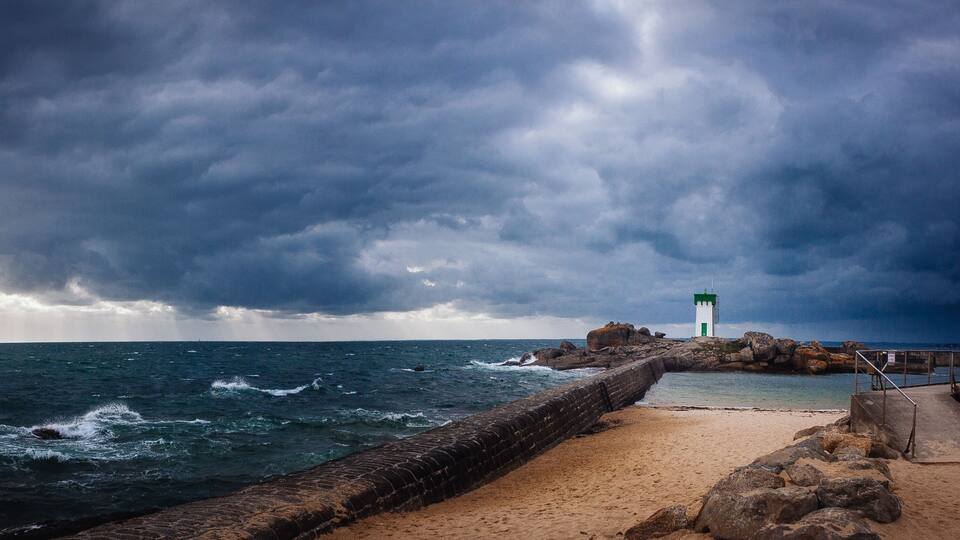 A rocky pier with a lighthouse, turbulent sea, and stormy sky.