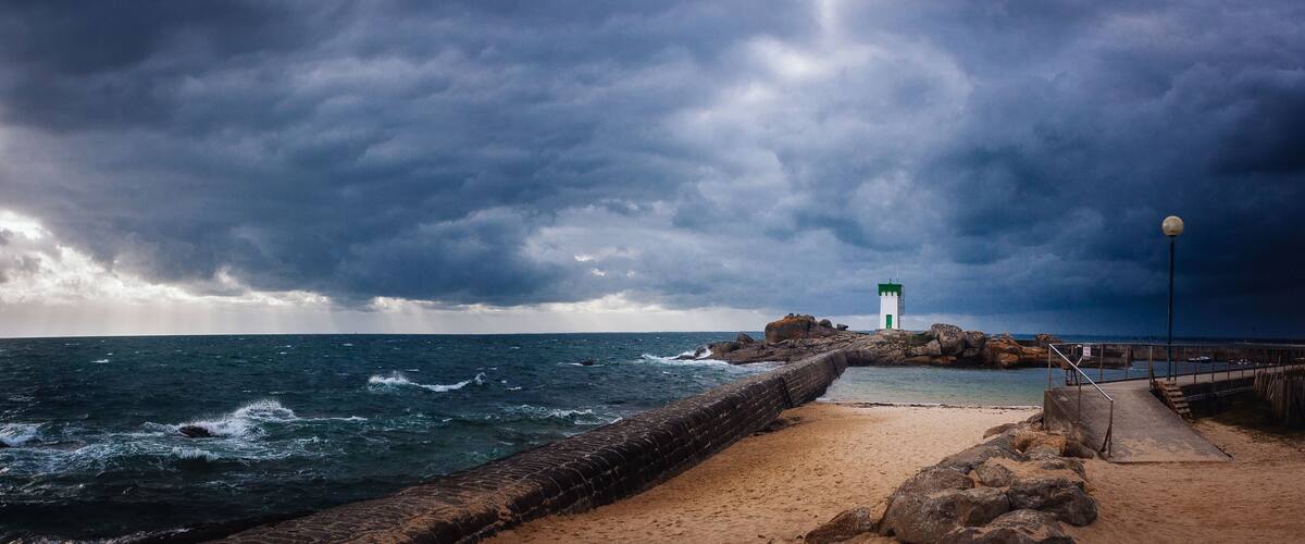 A rocky pier with a lighthouse, turbulent sea, and stormy sky.