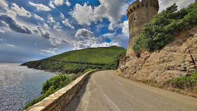 A coastal road with a stone wall and a castle tower.