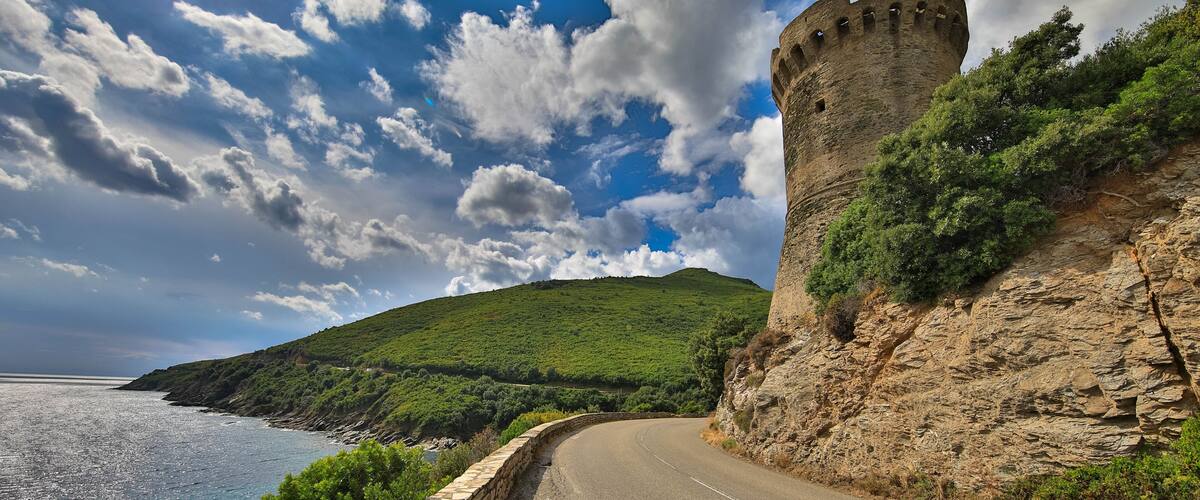 A coastal road with a stone wall and a castle tower.