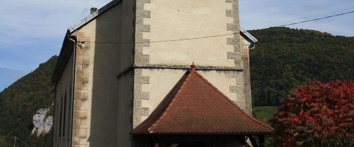 A church with a bell tower, surrounded by greenery and hills.