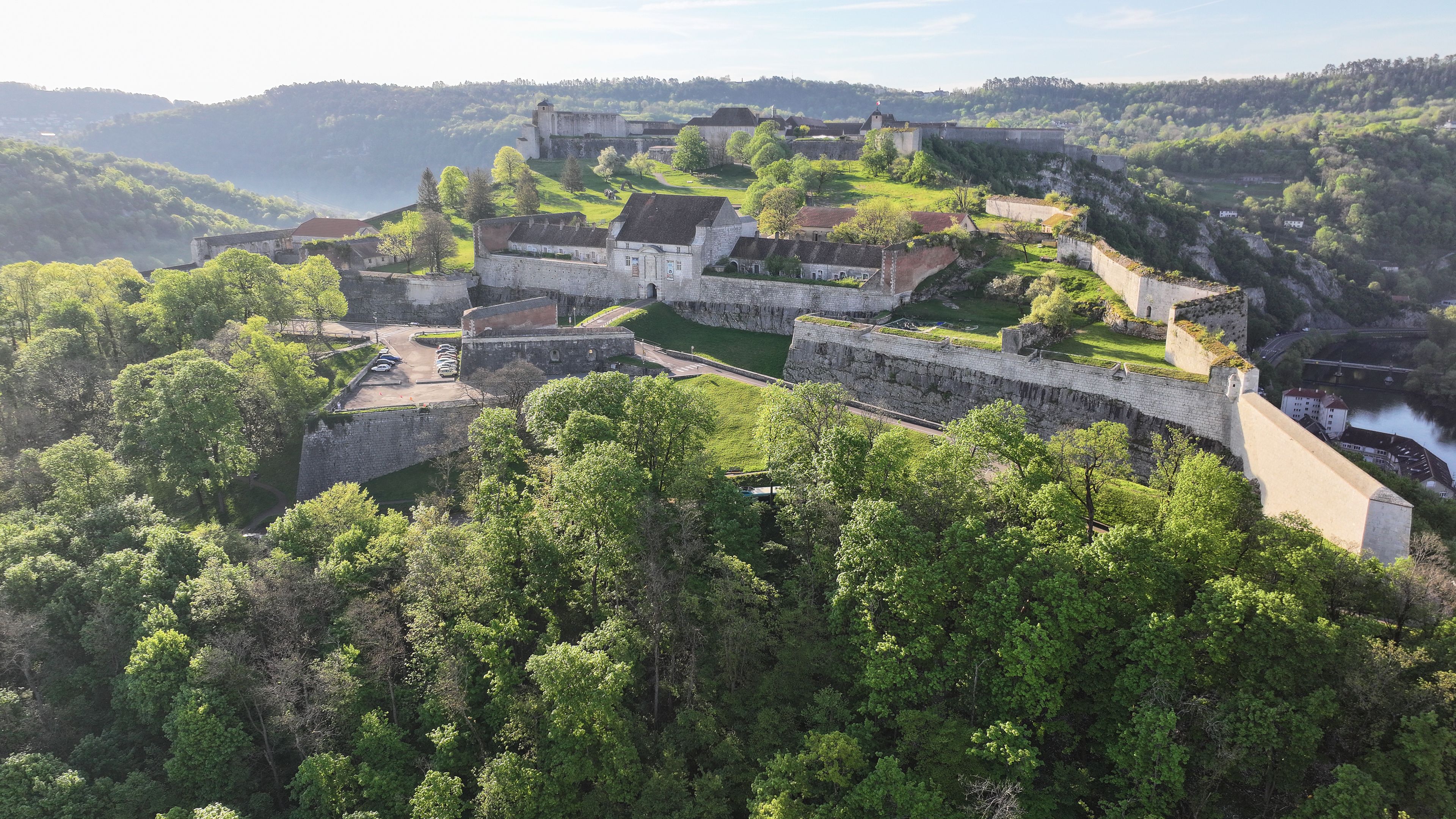 A medieval castle surrounded by lush greenery and hills.