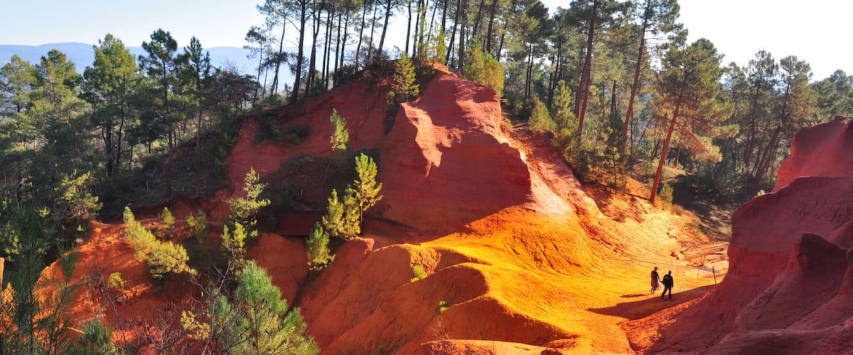 A red rock formation with a wooden walkway and pine trees.