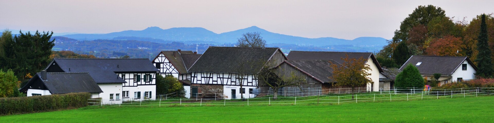 A rural landscape with houses, a green field, and mountains in the background.