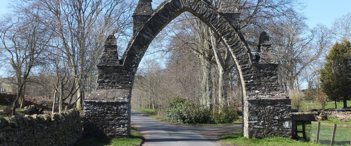 A stone archway with pointed tops, a paved road, and leafless trees in a rural setting.