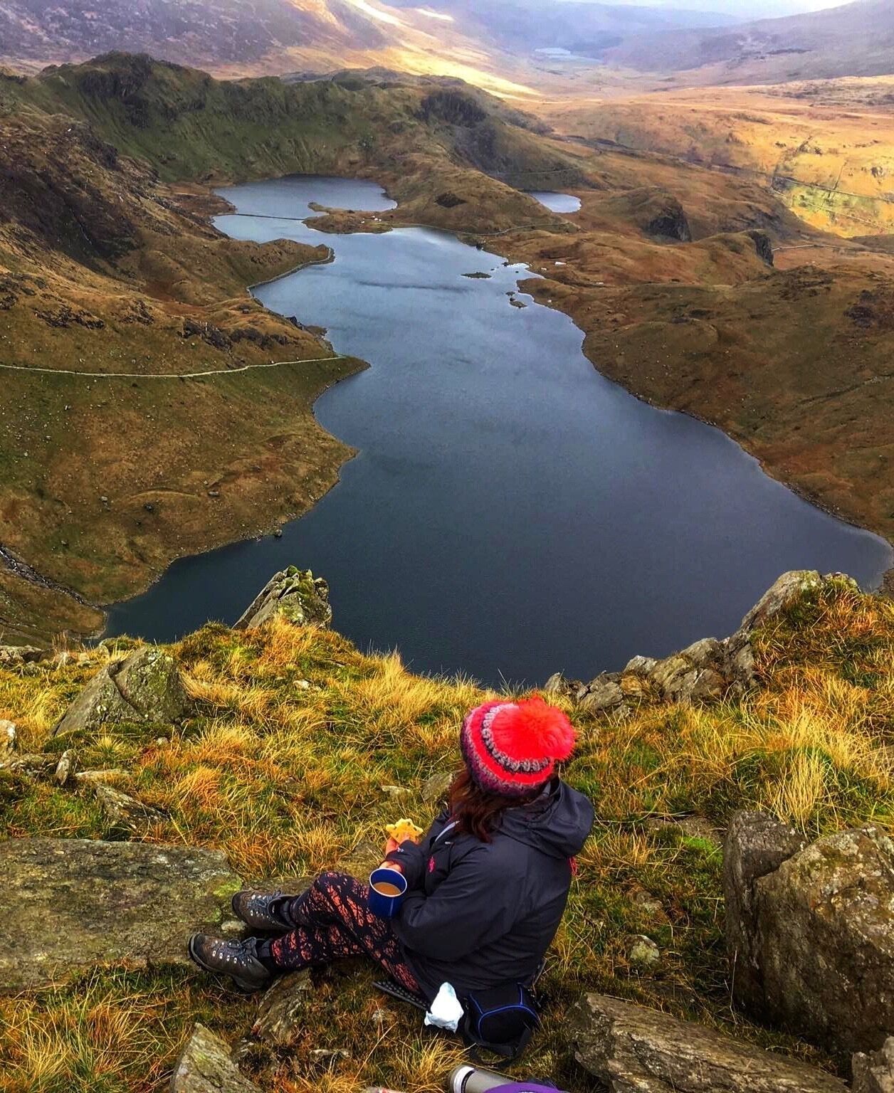 A person sitting on a grassy hill overlooking a lake surrounded by hills.