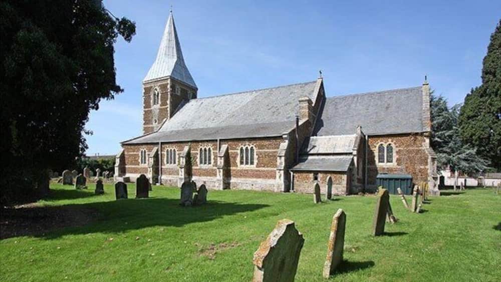 A church with a tall steeple and a graveyard in front.