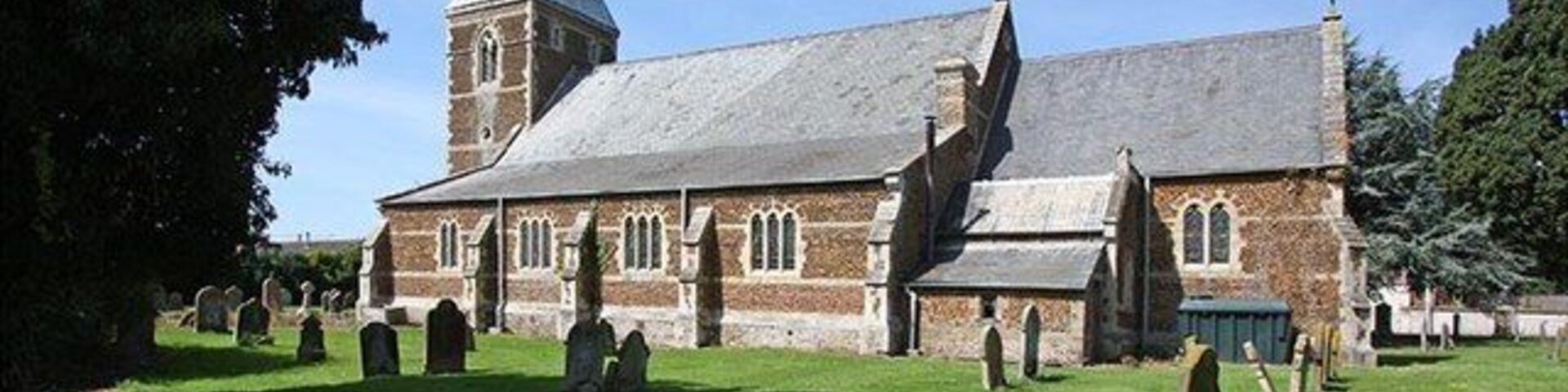Una iglesia con un campanario alto y un cementerio al frente.