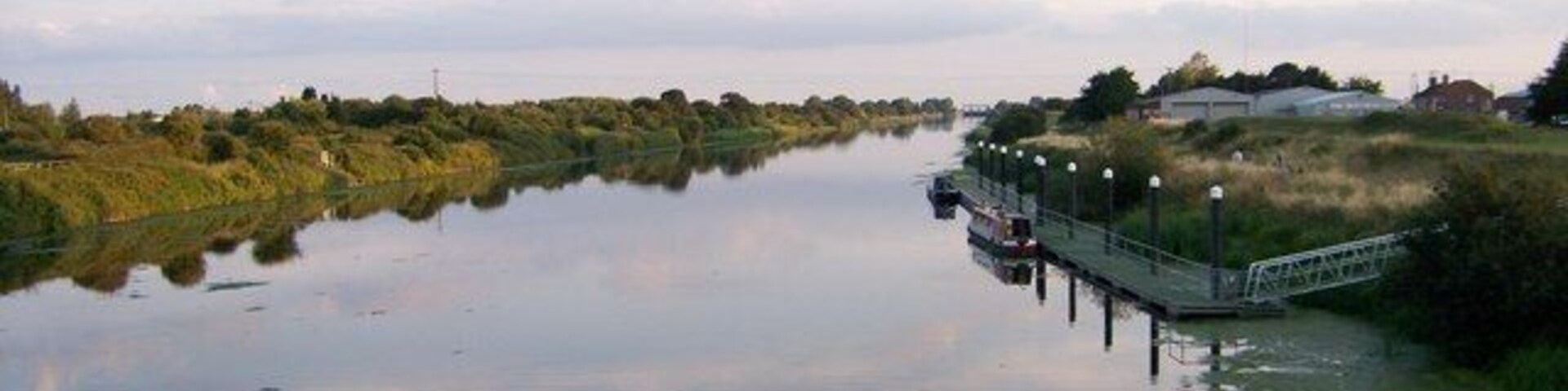 Um rio calmo com uma ponte e vegetação nas margens.