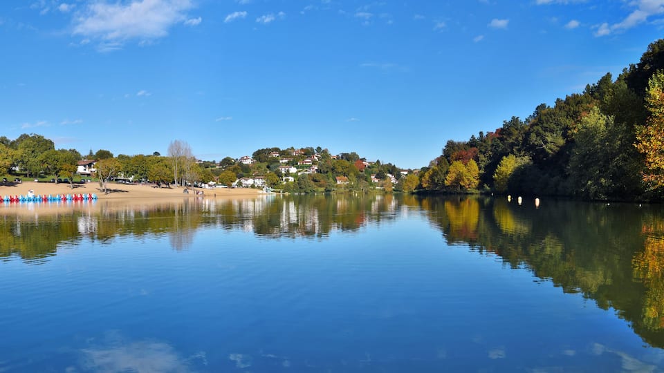 A calm river reflecting trees and buildings.