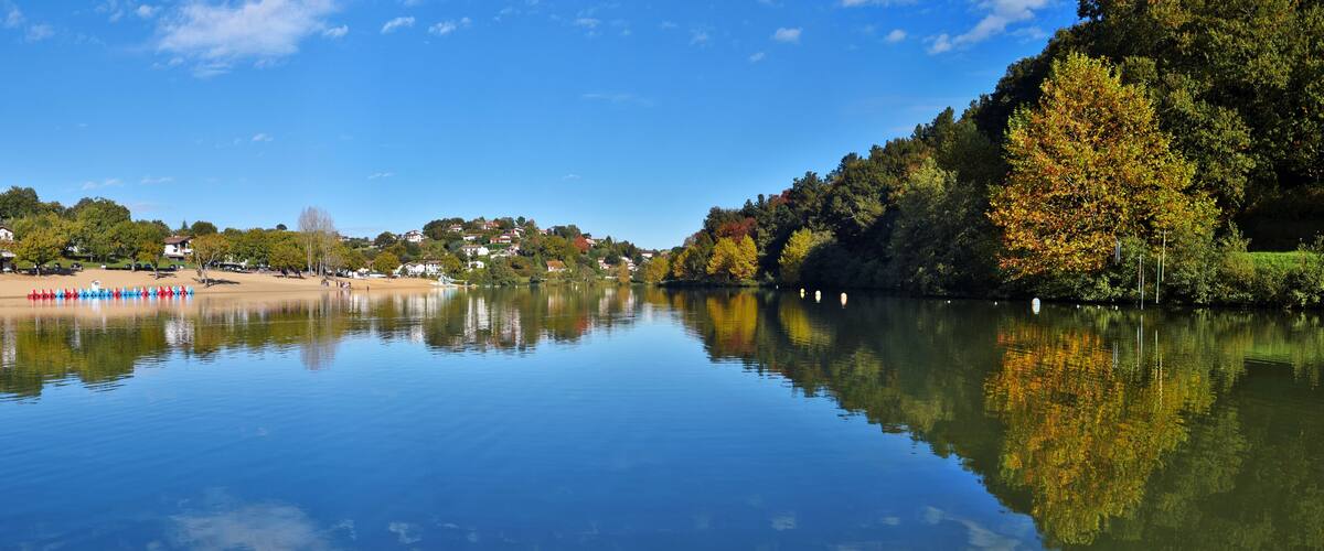 A calm river reflecting trees and buildings.