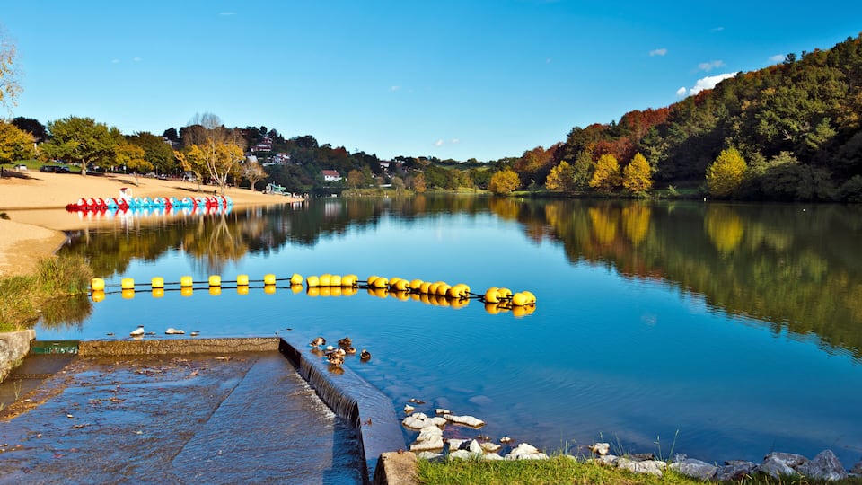 A calm lake with a dock, colorful paddle boats, and autumn trees reflecting on the water.