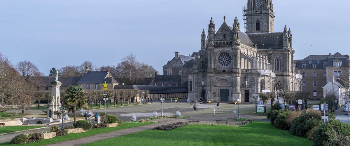 A historic church with a tall spire, a statue, and a well-maintained garden in front.
