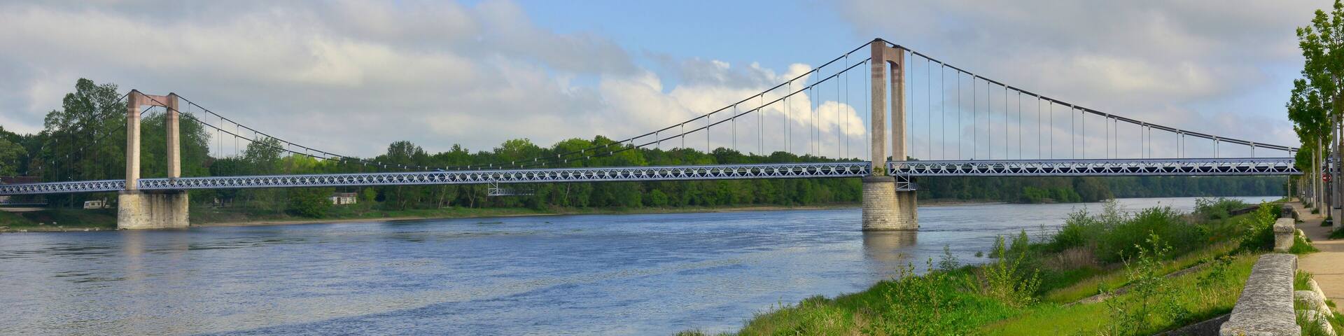 A suspension bridge over a river with greenery and trees in the background.