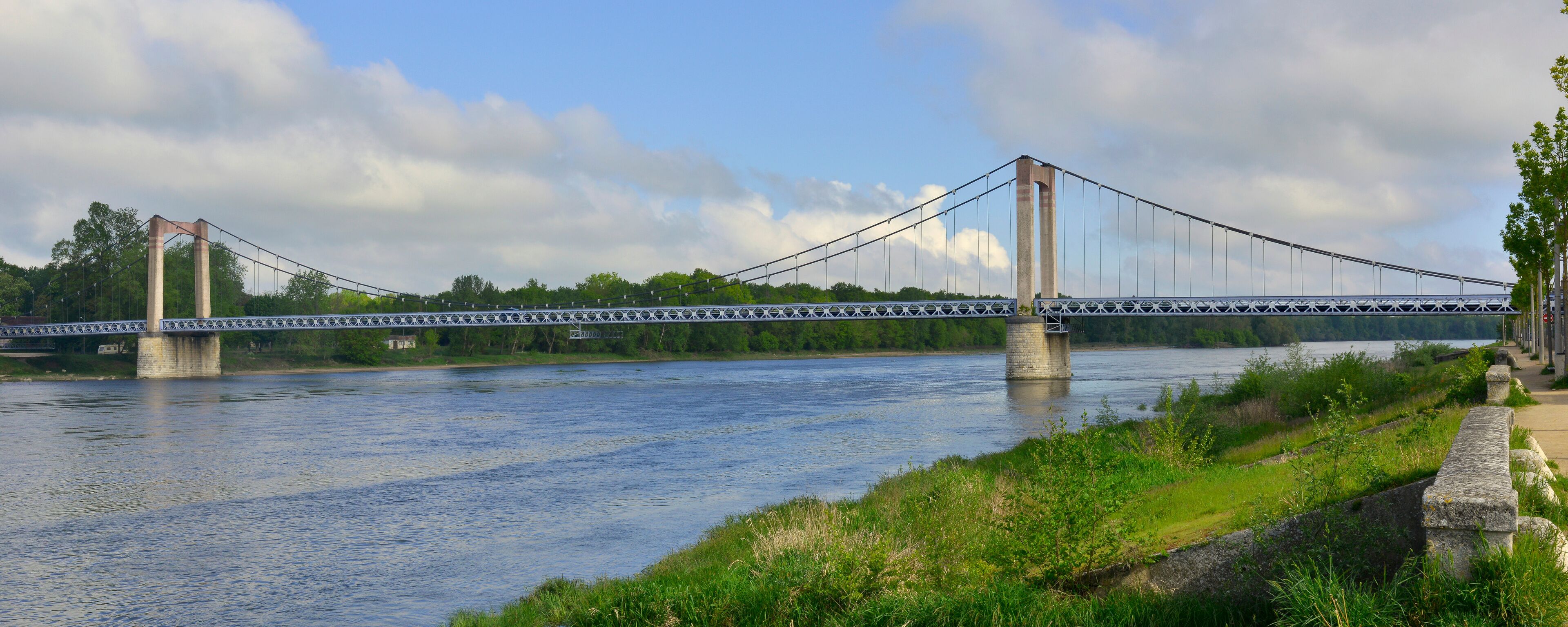 A suspension bridge over a river with greenery and trees in the background.